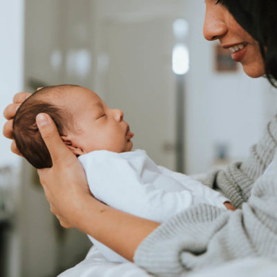 A woman admiring the young baby she holds in front of her.