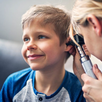 A smiling young boy is having his ear examined by a doctor with an otoscope.