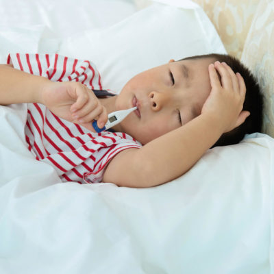 young boy holding his forehead and taking his temperature in bed
